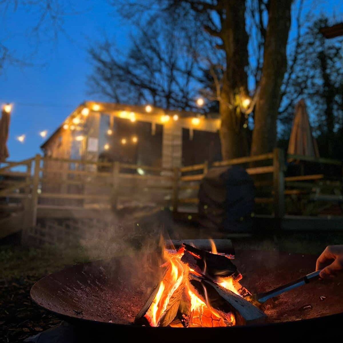 A person sitting by a campfire, grilling food on the fire, creating a cozy outdoor ambiance
