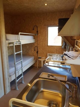 A cosy cabin with bunk beds and ladder and a compact kitchen area