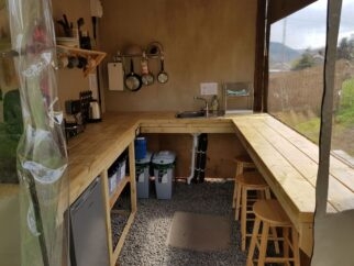 A simple camping kitchen with sink, hob, fridge, microwave and bar seating