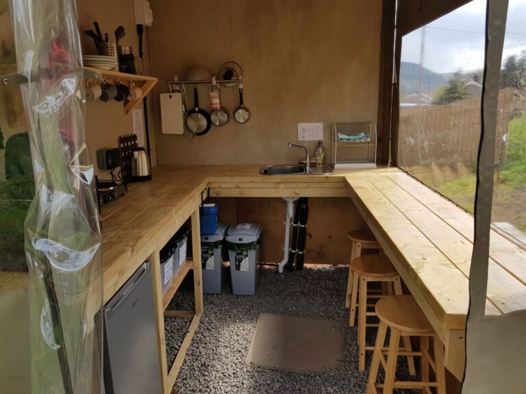 A simple camping kitchen with sink, hob, fridge, microwave and bar seating