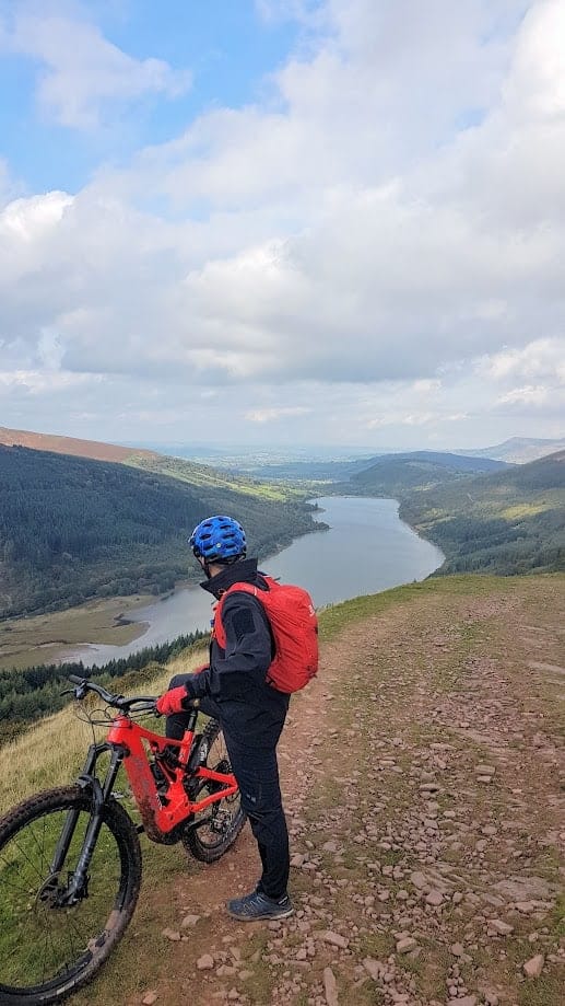 a man on a bike looking out over a reservoir with a cloudy sky 