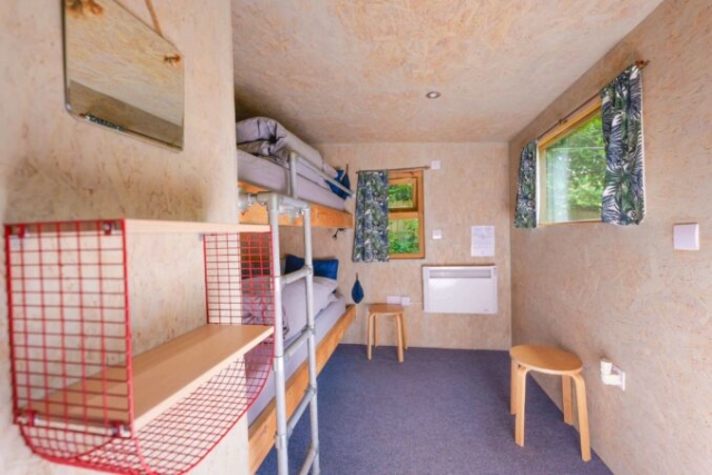 A cosy cabin interior with bunk beds and ladder, storage shelf and stools