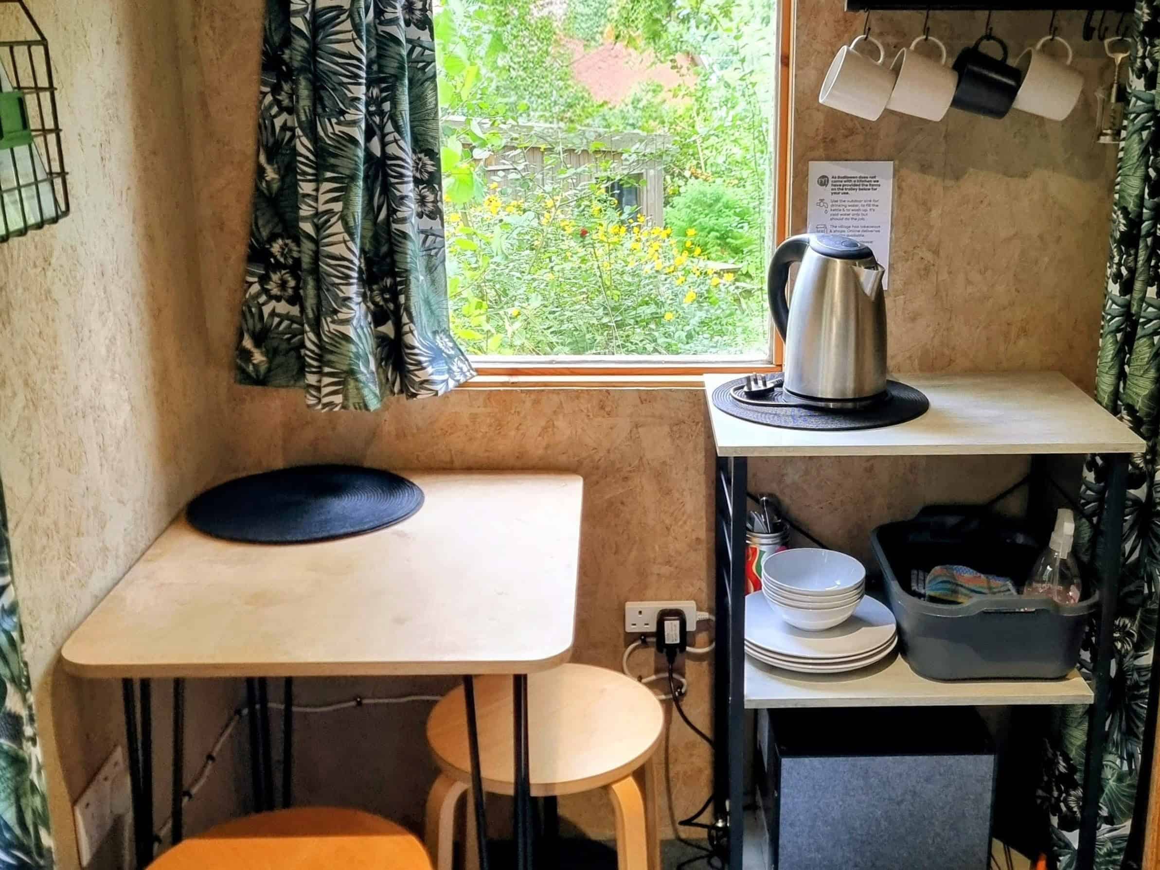 Bodlawen-kitchen-trolley A mini kitchen area with a kettle, cups, glasses, plates etc.